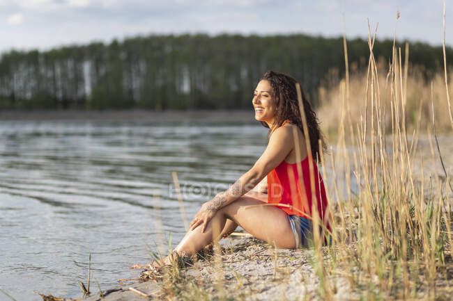 Portrait of happy young woman sitting at lakeshore — Stock Photo