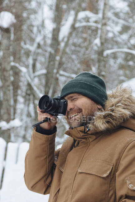 Retrato de homem relaxado tirando foto com câmera digital na floresta de inverno — Fotografia de Stock
