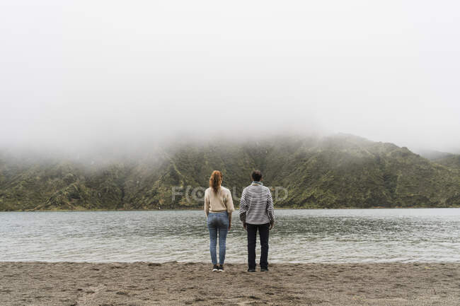 Vista trasera de la pareja en la orilla del lago explorando la isla de Sao Miguel juntos en Azores, Portugal - foto de stock