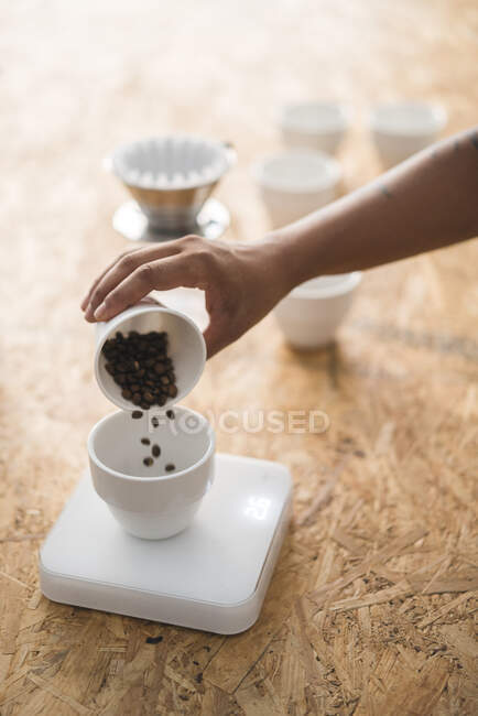 Primer plano de la mujer vertiendo granos de café en una taza - foto de stock
