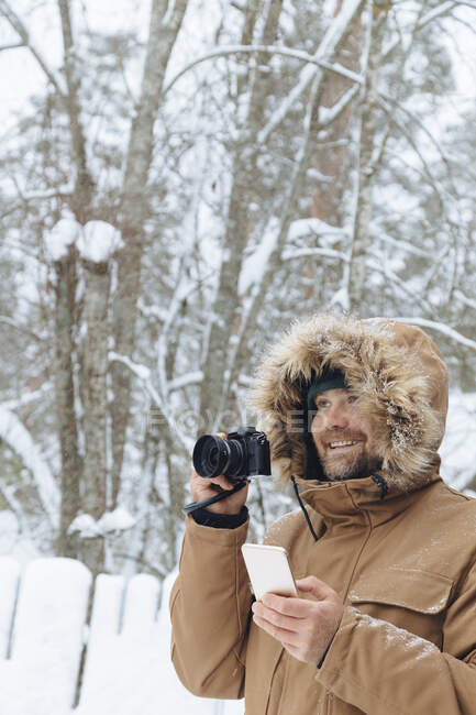 Портрет розслабленого чоловіка з цифровою камерою та мобільним телефоном у зимових лісах. — стокове фото