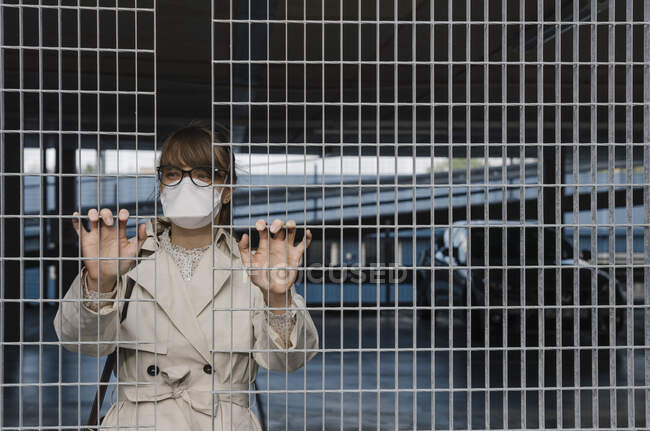 Femme portant un masque facial debout derrière une grille dans un parking — Photo de stock