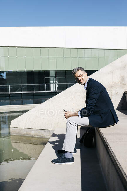 Homme d'affaires aux cheveux gris assis dans les escaliers d'une piscine — Photo de stock