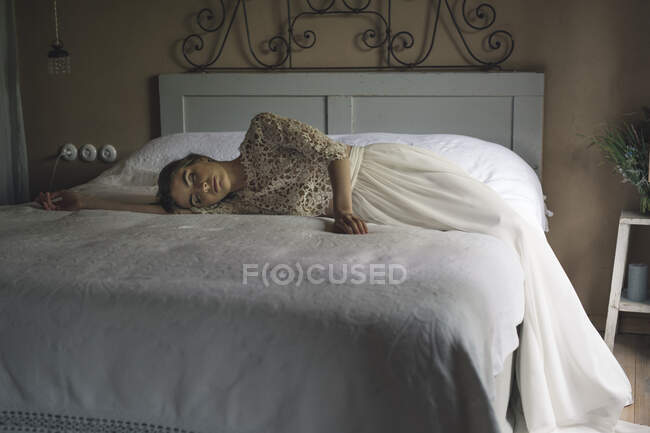 Jeune femme en robe de mariée couchée sur le lit — Photo de stock