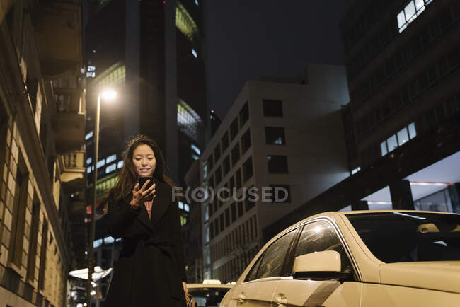 Young woman using smartphone in the city at night, Frankfurt, Germany — Stock Photo