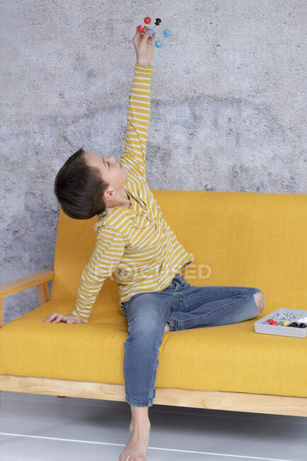 Boy joue et expérimente avec des modèles moléculaires assis sur un canapé jaune — Photo de stock