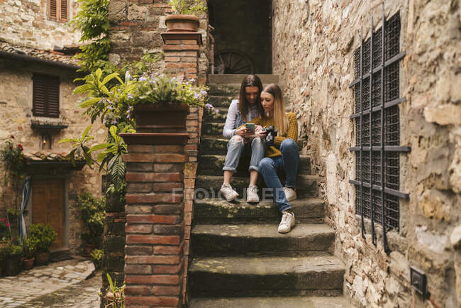 Duas jovens mulheres sentadas nas escadas olhando para o smartphone, Greve in Chianti, Toscana, Itália — Fotografia de Stock