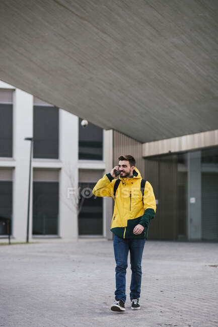 Sorrindo homem no telefone andando ao longo do edifício na cidade — Fotografia de Stock