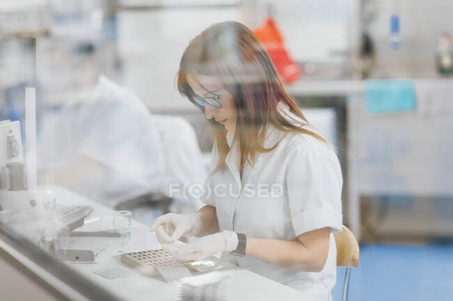 Técnico femenino seguro que se prepara para la investigación vista desde la ventana de vidrio - foto de stock
