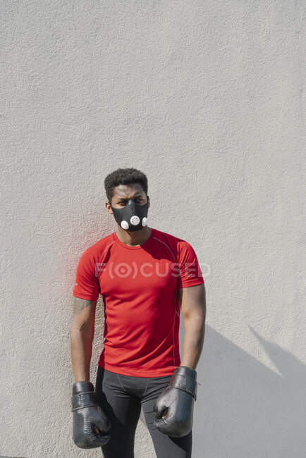 Retrato de um desportista usando máscara facial e luvas de boxe em uma parede — Fotografia de Stock