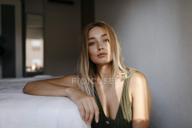 Seductive young woman sitting by bed in bedroom at home — Stock Photo