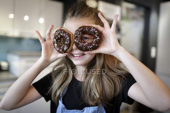 Portrait of smiling girl looking through doughnuts — Stock Photo