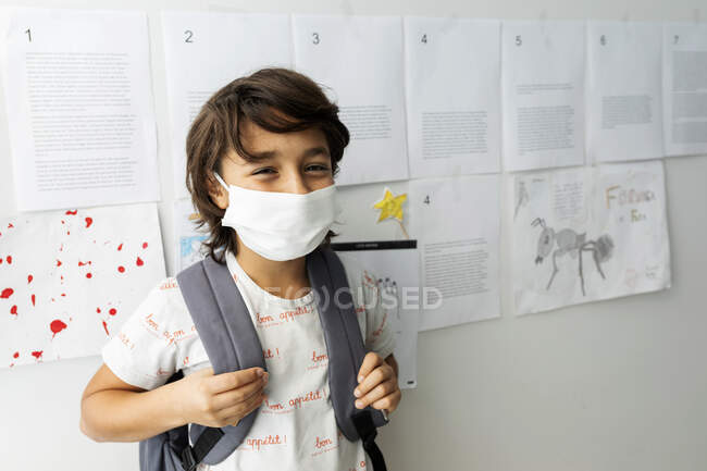 Хлопчик у масці стоїть навпроти паперів, що стоять на стіні в школі. — стокове фото