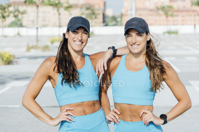 Ritratto di sorridente fiduciosa giovane gemelle in abbigliamento sportivo in piedi all'aperto nella giornata di sole — Foto stock