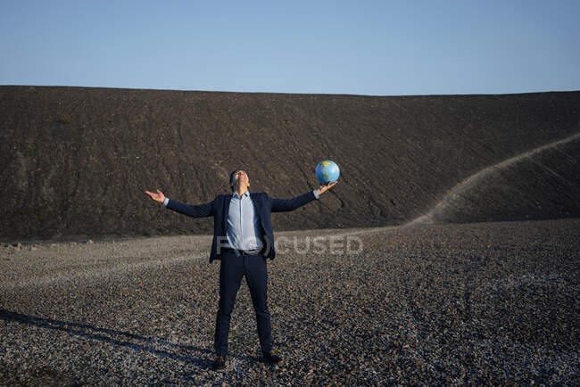 Reifer Geschäftsmann hält einen Globus auf einer stillgelegten Minenspitze — Stockfoto