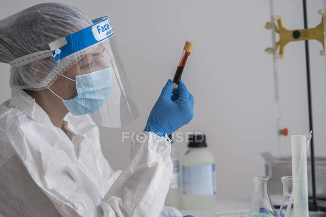 Donna in abbigliamento protettivo seduta alla scrivania esaminando il campione di sangue — Foto stock