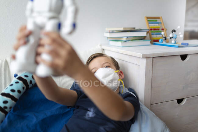 Мальчик в маске играет в своей комнате во время коронного кризиса со своим новым, единственным другом, роботом — стоковое фото