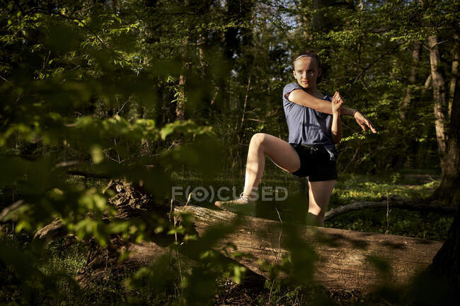 Full length of girl stretching arm on fallen tree in forest — Stock Photo