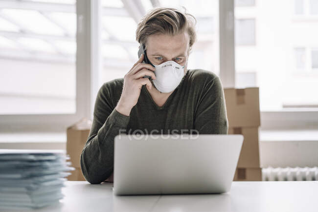 Businessman wearing protective mask and using laptop and cell phone — Stock Photo