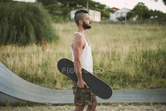 Handsome young man holding skateboard looking away while standing on land — Stock Photo