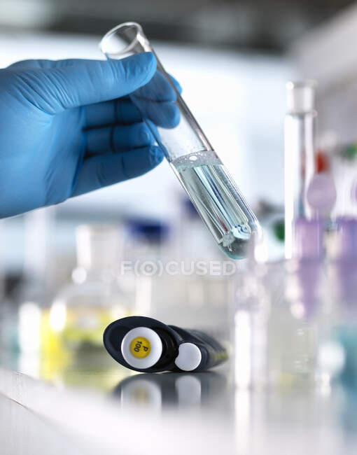 Mano recortada de científico masculino mezclando fórmula química en tubo de ensayo para experimento en laboratorio - foto de stock