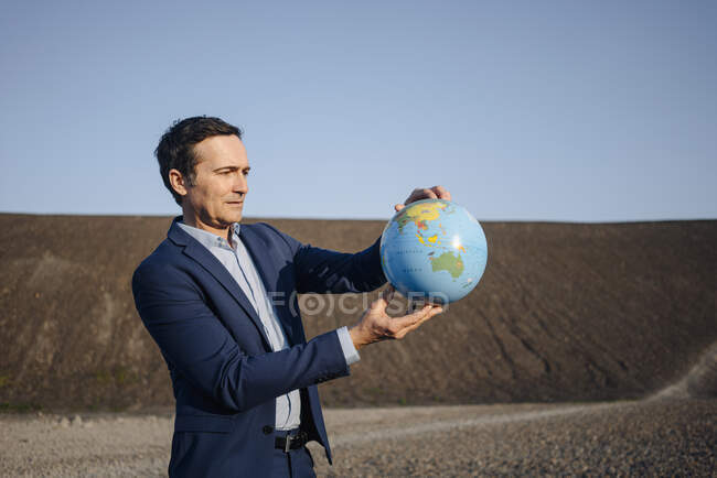 Reifer Geschäftsmann hält einen Globus auf einer stillgelegten Minenspitze — Stockfoto