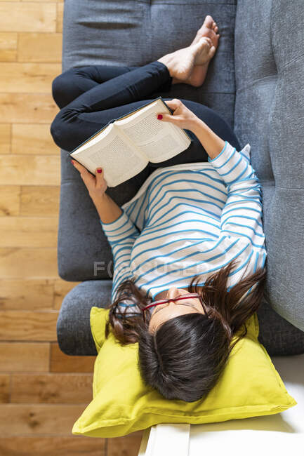 Жінка відпочиває на дивані і читає книжку. — стокове фото