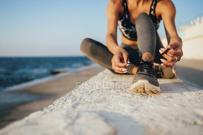Sezione bassa di giovane donna che lega lacci da scarpe sul lungomare — Foto stock