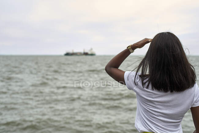 Back view of young woman in front of the sea looking to ship at horizon — Stock Photo