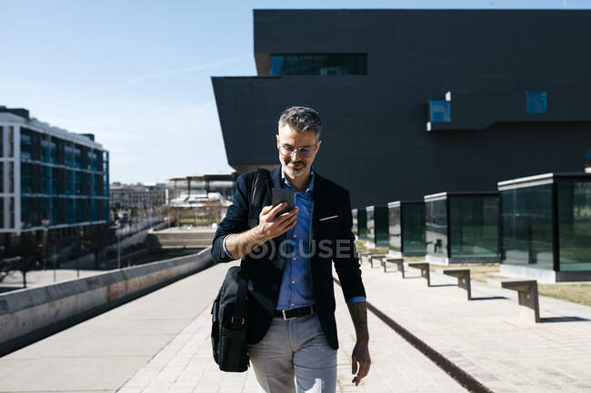 Сіроволосий бізнесмен ходить з мобільним телефоном у місті. — стокове фото
