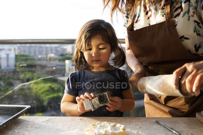 Retrato de una niña horneando galletas con su madre - foto de stock
