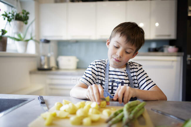 Портрет маленького хлопчика, що ріже картоплю на кухні — стокове фото