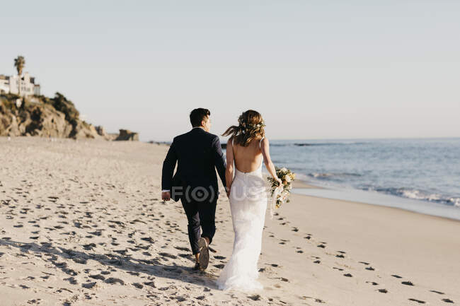 Rückansicht eines glücklichen Brautpaares beim Laufen am Strand — Stockfoto