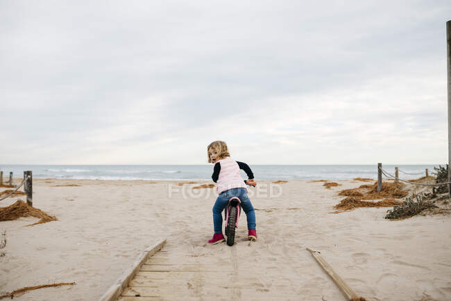 Rear view of toddler girl with balance bicycle on a boardwalk in the dunes — Stock Photo
