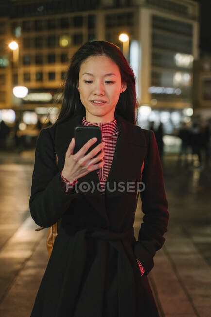 Jovem mulher usando smartphone na cidade à noite, Frankfurt, Alemanha — Fotografia de Stock