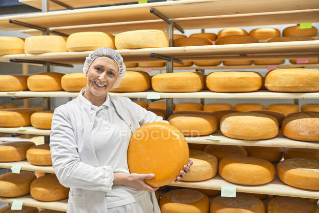 Fromagerie, travailleuse souriante tenant une meule de fromage — Photo de stock
