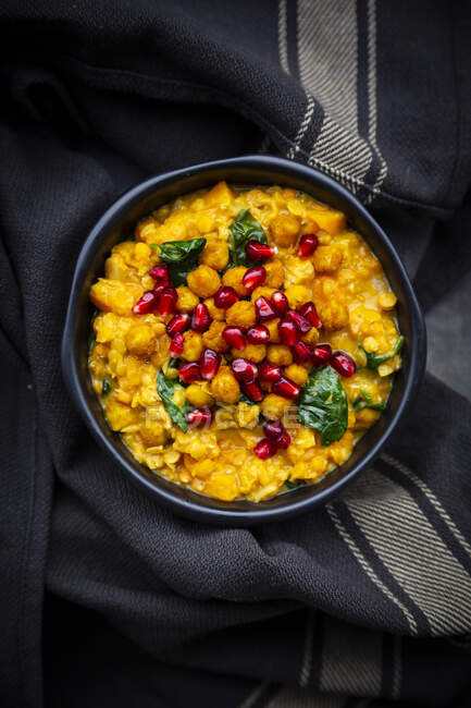 Bowl of vegan curry with red lentils, sweet potatoes, spinach, roasted turmeric chick-peas, pomegranate seeds and cilantro — Stock Photo