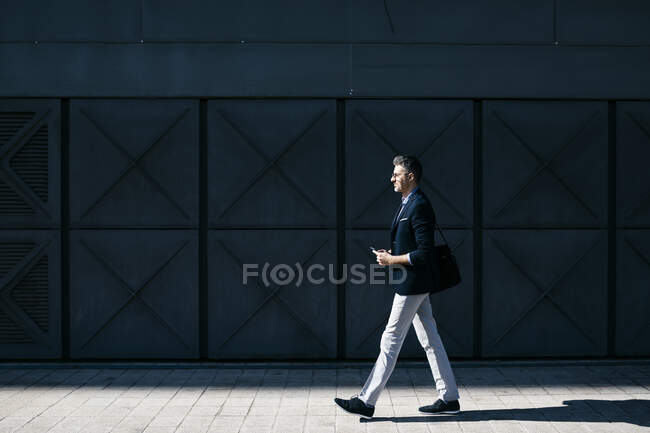 Uomo d'affari dai capelli grigi che cammina lungo un edificio in città — Foto stock