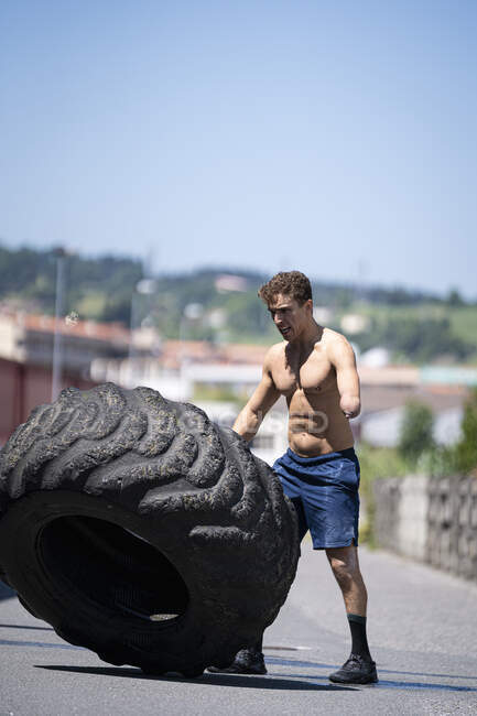 Спортсмен с ампутированной рукой, тренирующийся с тракторной шиной на дороге — стоковое фото