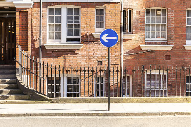 Reino Unido, Londres, Edificio de ladrillo en camino vacío durante el toque de queda en el barrio de Bloomsbury con una flecha azul - foto de stock