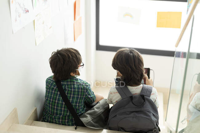 Ragazzi che indossano maschere parlando mentre seduti su gradini a scuola — Foto stock