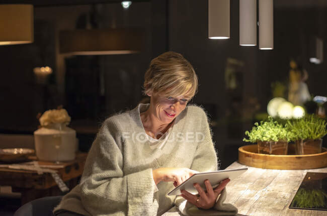 Посмішка блондинки працює пізно, використовуючи цифрові таблетки в освітленій вітальні. — стокове фото
