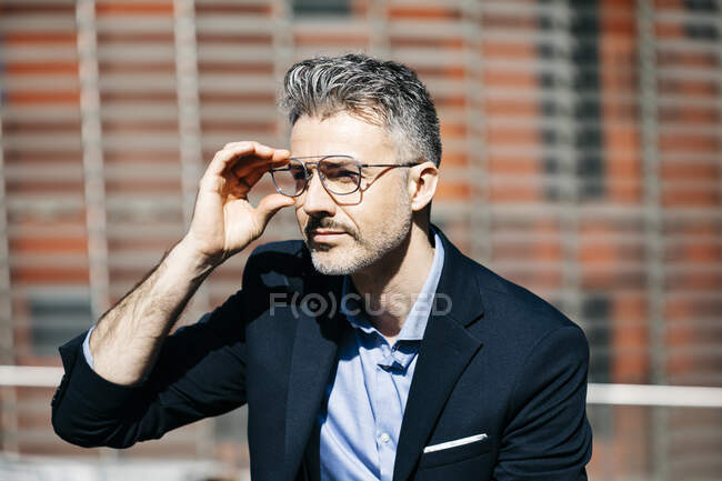 Ritratto di un uomo d'affari dai capelli grigi in città che si mette gli occhiali — Foto stock