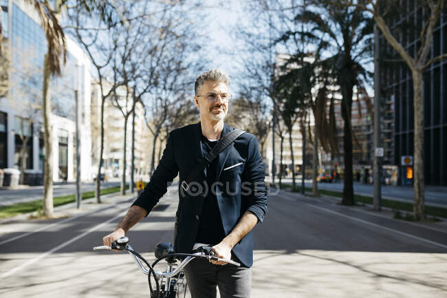 Сіроволосий бізнесмен штовхає свій велосипед у місті. — стокове фото