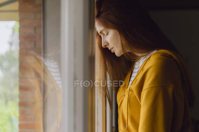 Рыжая женщина с закрытыми глазами прислонилась к окну — стоковое фото