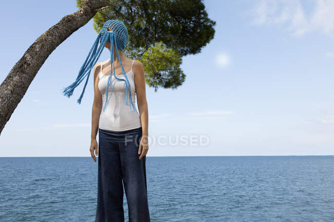 Mujer con tocado azul de ganchillo con flecos de pie frente al mar - foto de stock