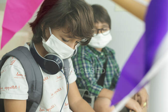 Хлопчики в масках підтримують соціальну дистанцію, сидячи в школі. — стокове фото