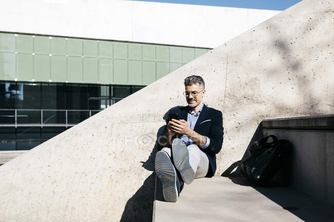 Uomo d'affari dai capelli grigi seduto sulle scale usando il cellulare — Foto stock
