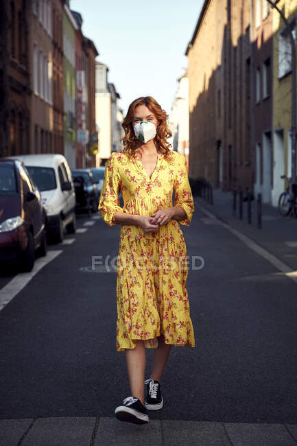 Donna dai capelli rossi che indossa una maschera viso FFP2 e cammina su strada vuota — Foto stock
