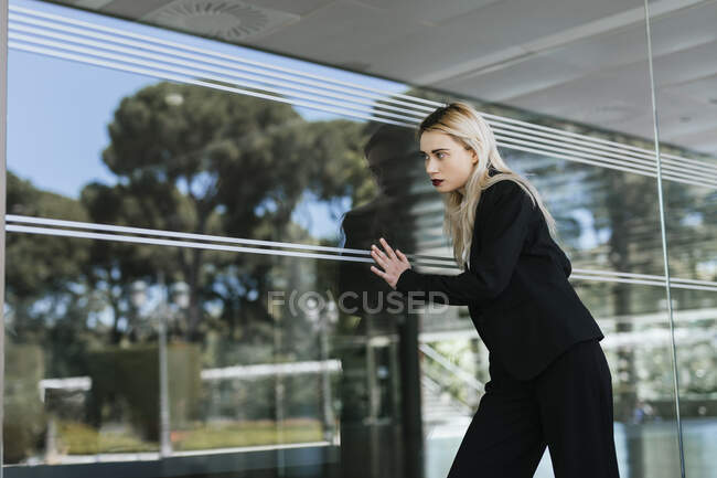 Portrait of young businesswoman wearing black pantsuit standing in front of glass pane — Stock Photo